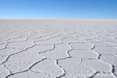 Die Salzkruste des Salar de Uyuni bricht in hexagonalen Formen auf und zieht sich bis zum Horizont hin.